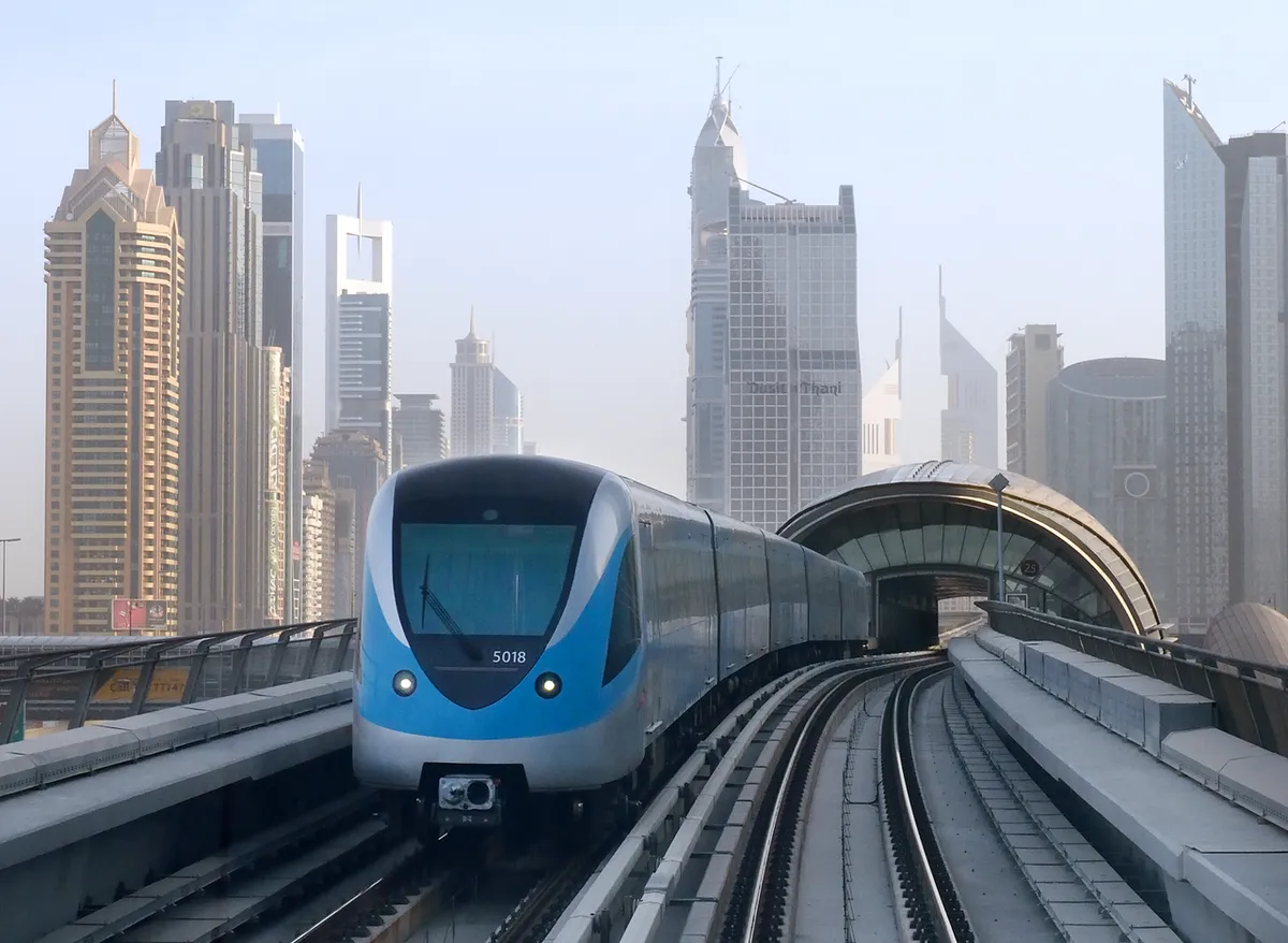 A blue and silver Dubai Metro train on an elevated track among skyscrapers