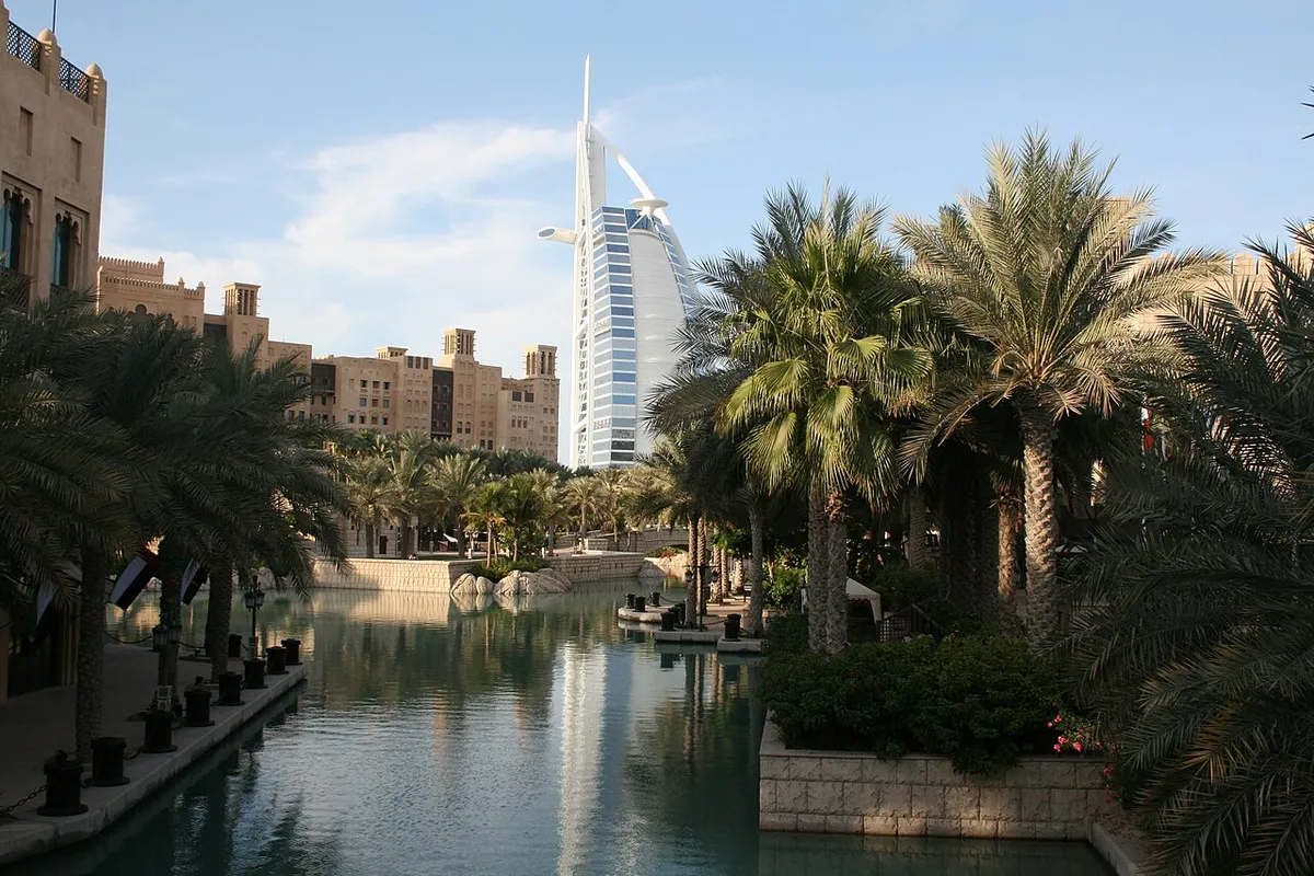 Madinat Jumeirah's sand-coloured buildings and palm trees beside a waterway, with the Burj Al Arab behind