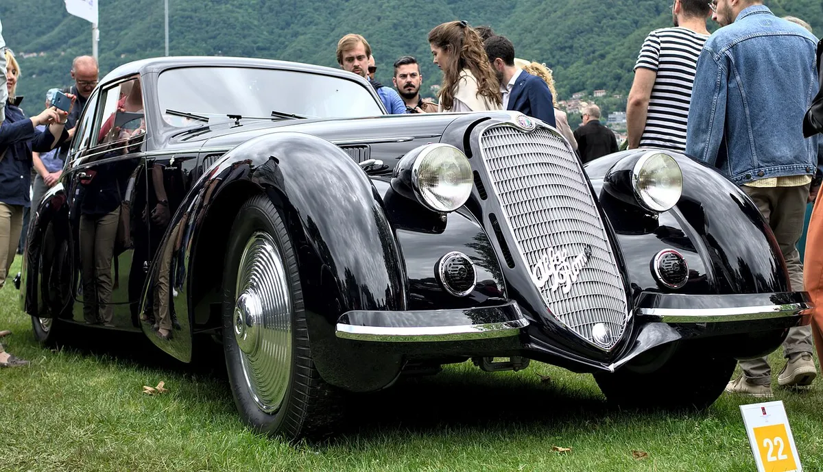 A black Alfa Romeo 8C 2900B coupé on the lawn with visitors around it beside Lake Como