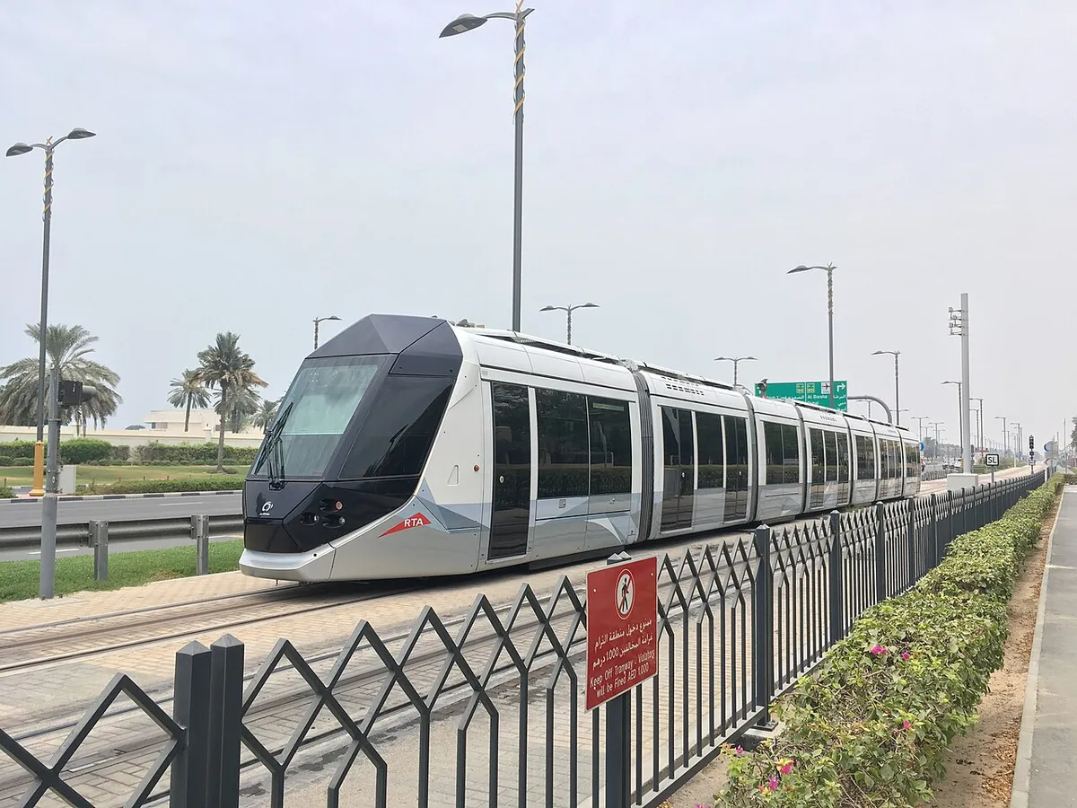 A silver Dubai Tram running beside a road lined with palm trees