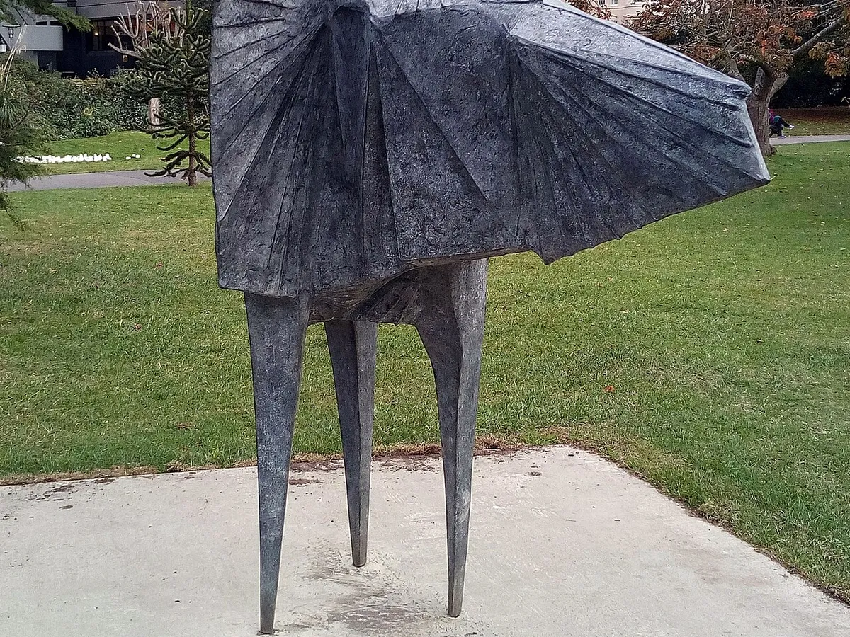 A bronze figure sculpture with a wide cloak standing on a plinth on the lawn in Regent's Park