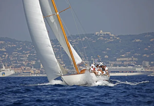 A white classic yacht with a wooden mast heeling under full sail in choppy blue water
