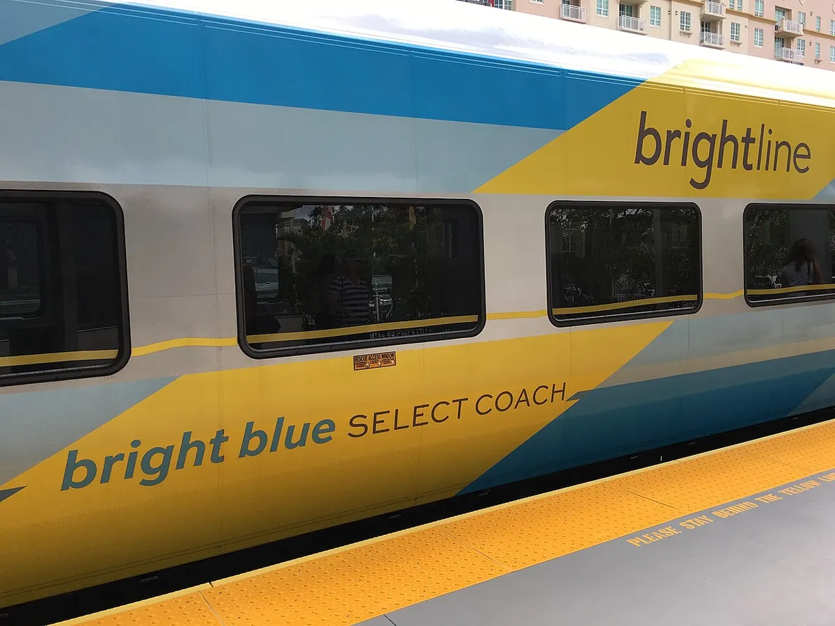 The side of a yellow, blue and grey Brightline train at a station platform