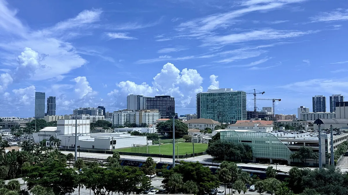 Downtown West Palm Beach office towers and palm trees under a blue sky with tall clouds