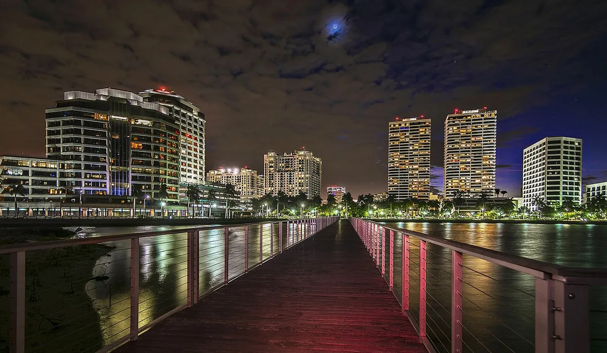 A lit pier stretching across the Intracoastal Waterway towards the West Palm Beach skyline at night