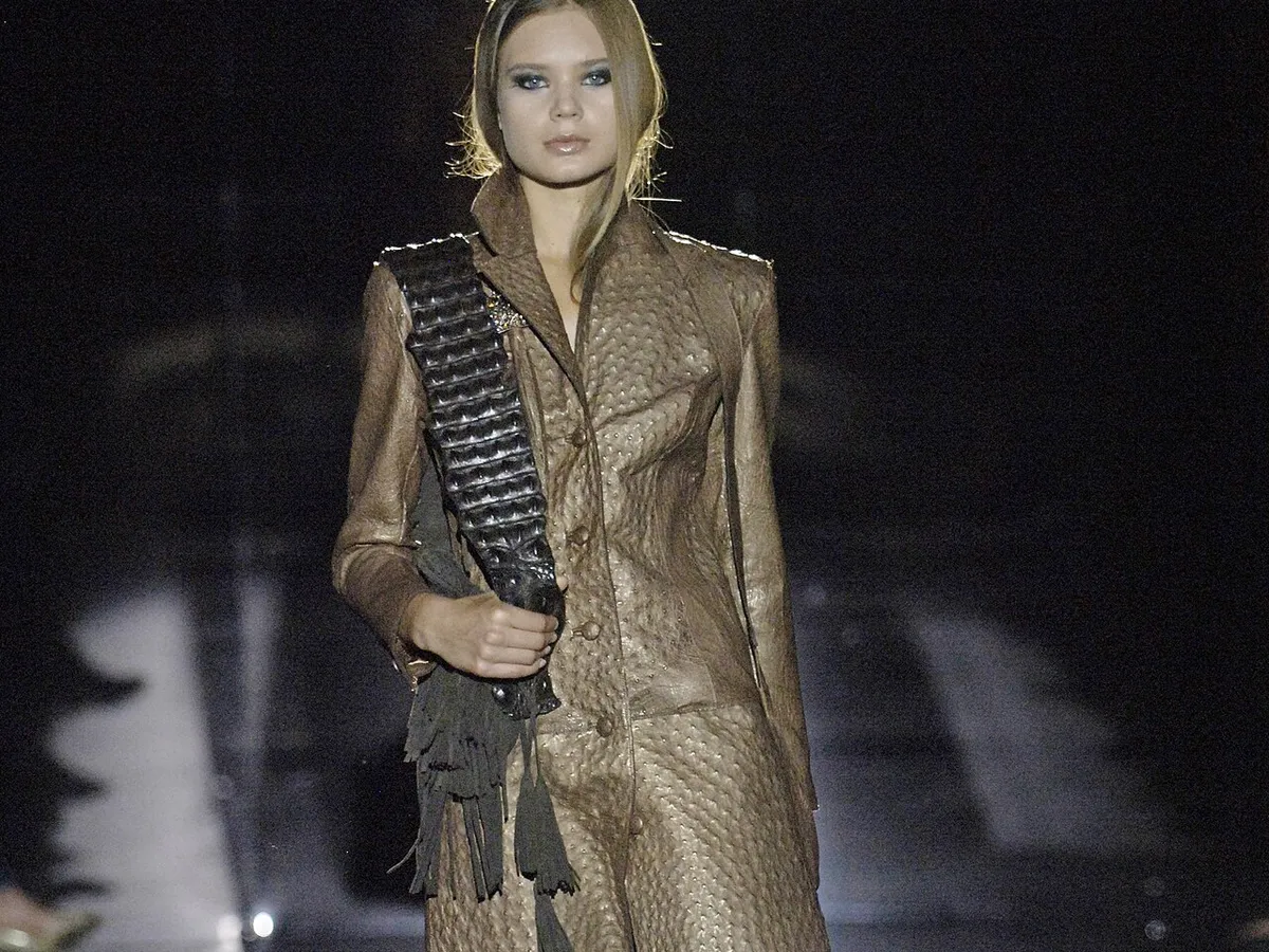 A model on a dark runway wearing a bronze textured coat and trousers