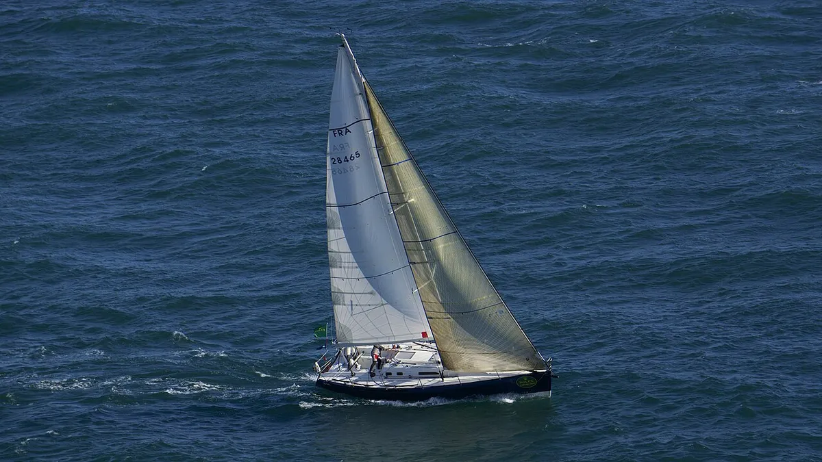 A racing yacht with a black and white mainsail heeling across dark blue water