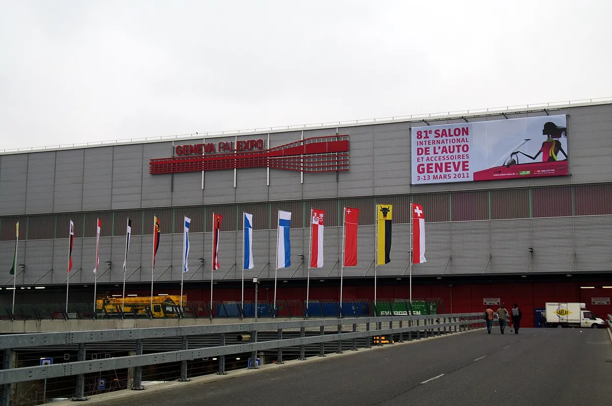 The long grey facade of Palexpo in Geneva with a row of national flags in front